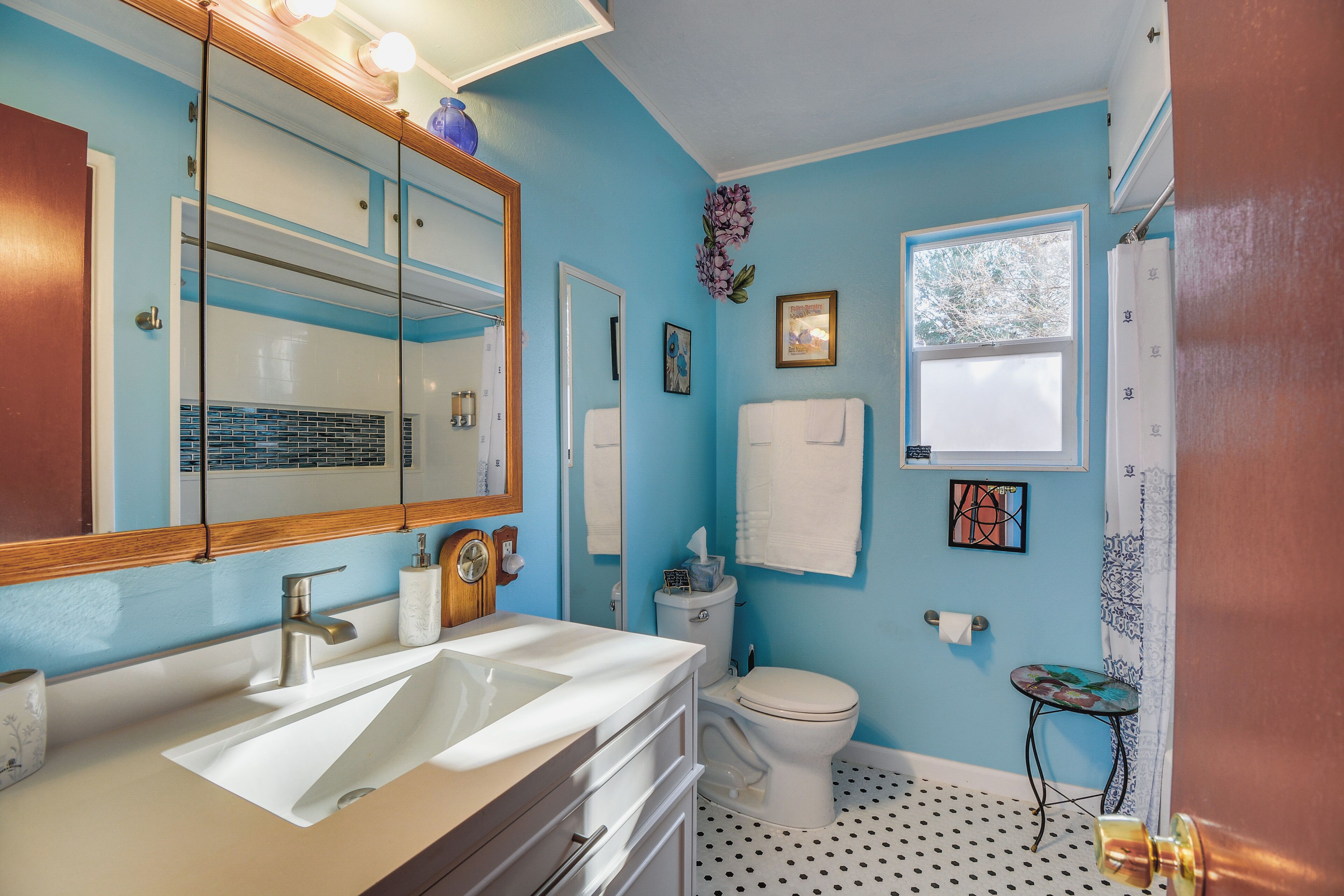 Een badkamer met een grote spiegel, twee wastafels, een toilet en een klein tafeltje.