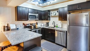 A modern kitchen with dark cabinets, stainless steel appliances, a granite countertop, and a skylight. - Ski-in, Ski-out Brian Head Condo w/ Fireplace! (Brian Head)