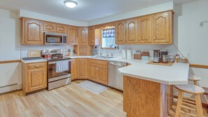 Una cocina con armarios de madera, microondas, horno, lavaplatos y una barra con taburetes.