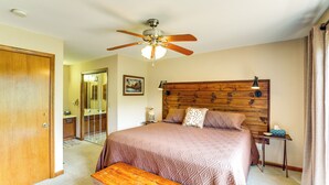 A bedroom with a wooden headboard, a ceiling fan, a bedside table with a lamp, and a wooden bench. - Maggie Valley Mountain Escape w/ Fireplace & Deck! (Maggie Valley)