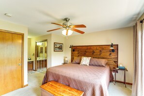 A bedroom with a wooden headboard, a bed with patterned bedding, a ceiling fan, a bedside table with a lamp, and a wooden bench. - Maggie Valley Mountain Escape w/ Fireplace & Deck! (Maggie Valley)