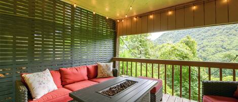 An outdoor seating area with a sofa, a table, and a view of a forested landscape.