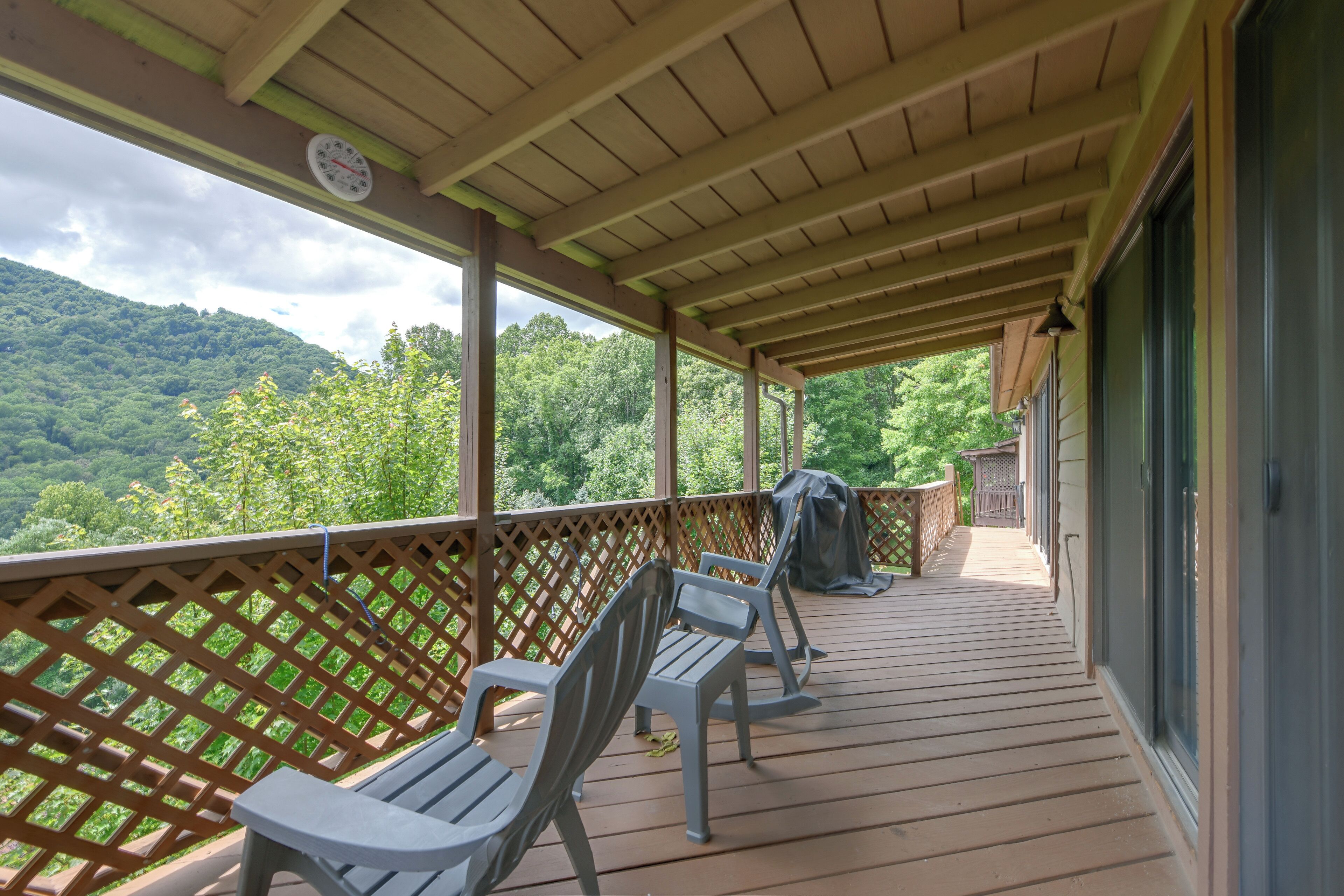 A covered deck with wooden railings, a view of a forested mountain, and a grill.