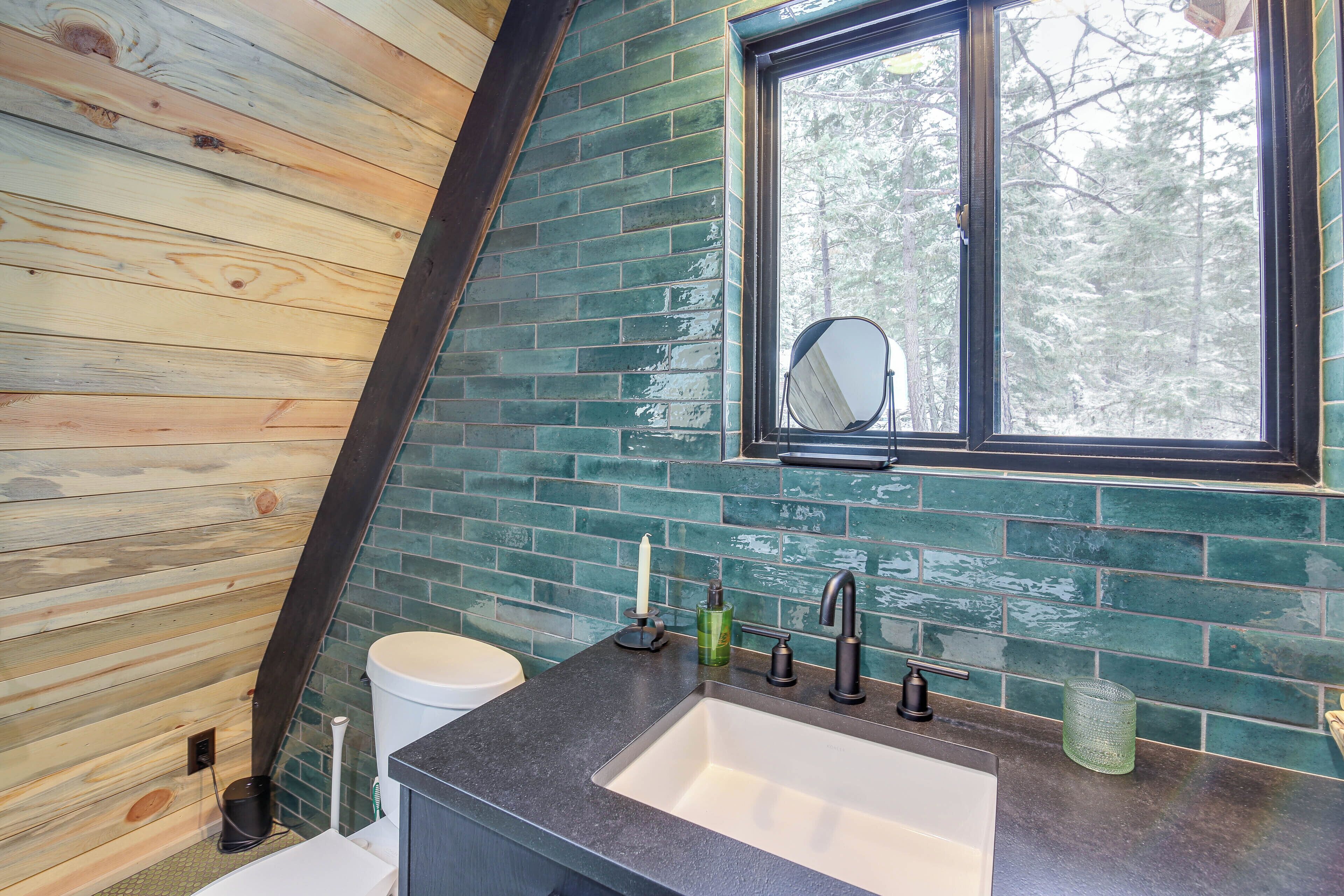 Une salle de bain avec un plafond en pente en bois, un lavabo avec un robinet noir et une fenêtre avec un miroir.