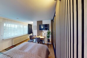 A modern hotel room with a large bed, a desk with two chairs, a TV, and a potted plant. - Crown Studio Dornbirn - Terrasse - Parkplatz (Dornbirn)