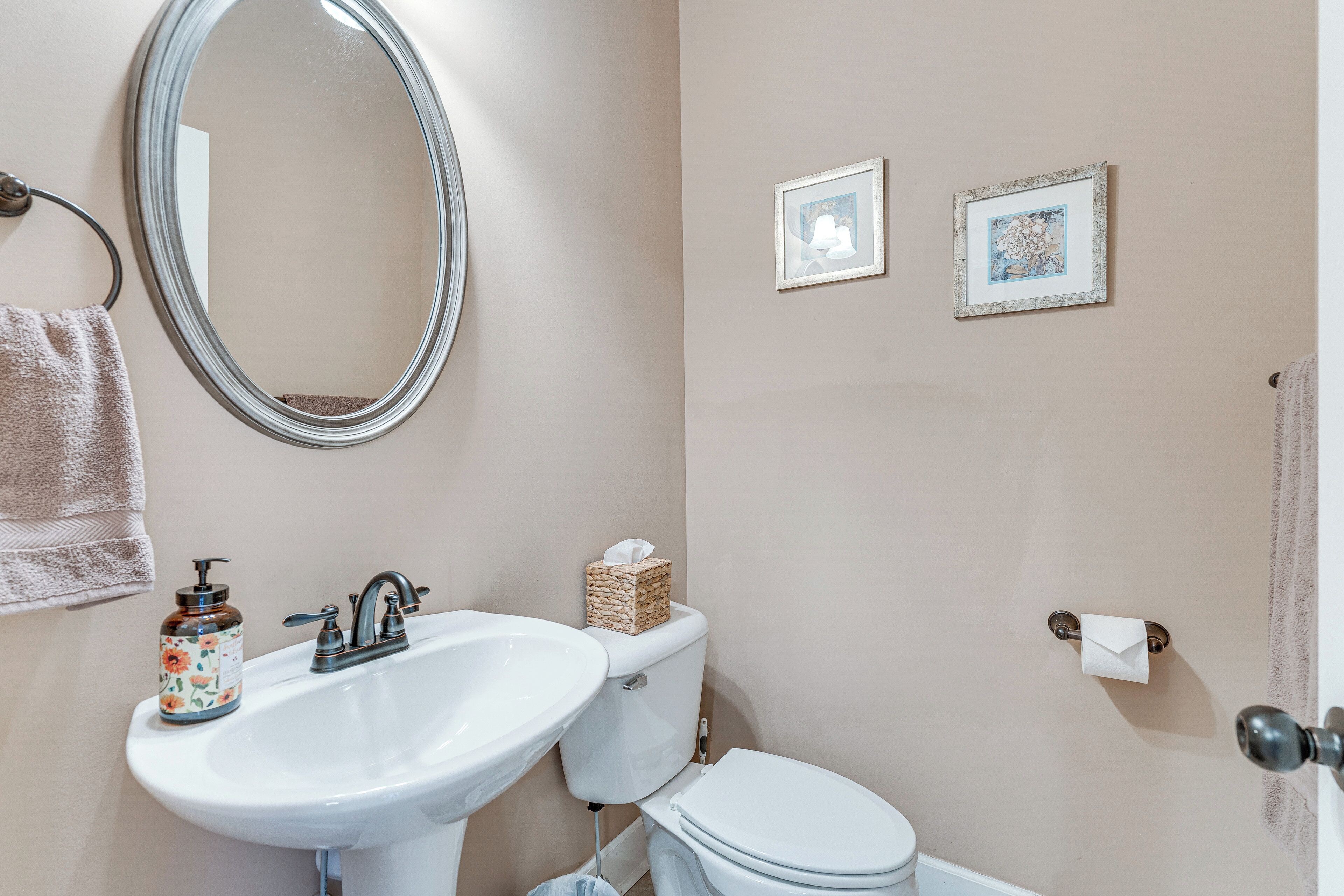 Une salle de bain avec un lavabo, des toilettes et un miroir. Deux tableaux encadrés sont accrochés au mur.