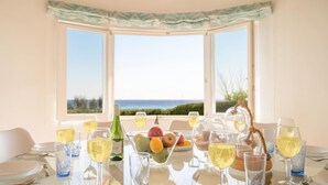 A table set for dining with a view of the sea, a bottle of wine, and a bowl of fruit.