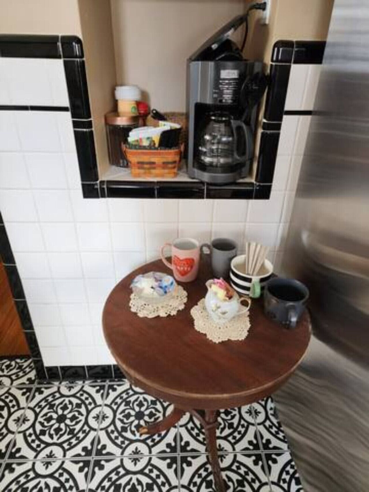 A kitchen with a coffee maker, a coffee pot, and a small table with cups and a teapot.