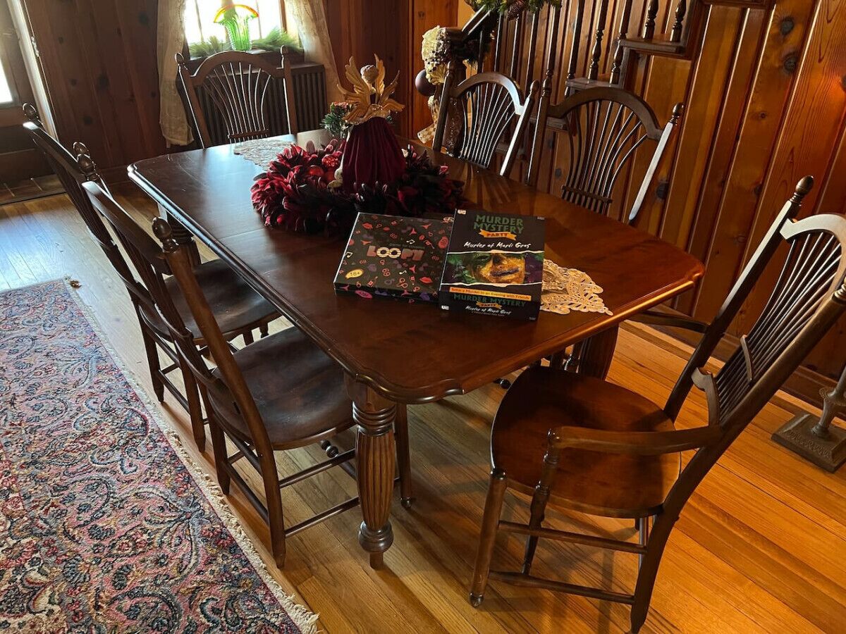 A wooden dining table with chairs, a decorative wreath, and two books titled "Murder Mysteries."