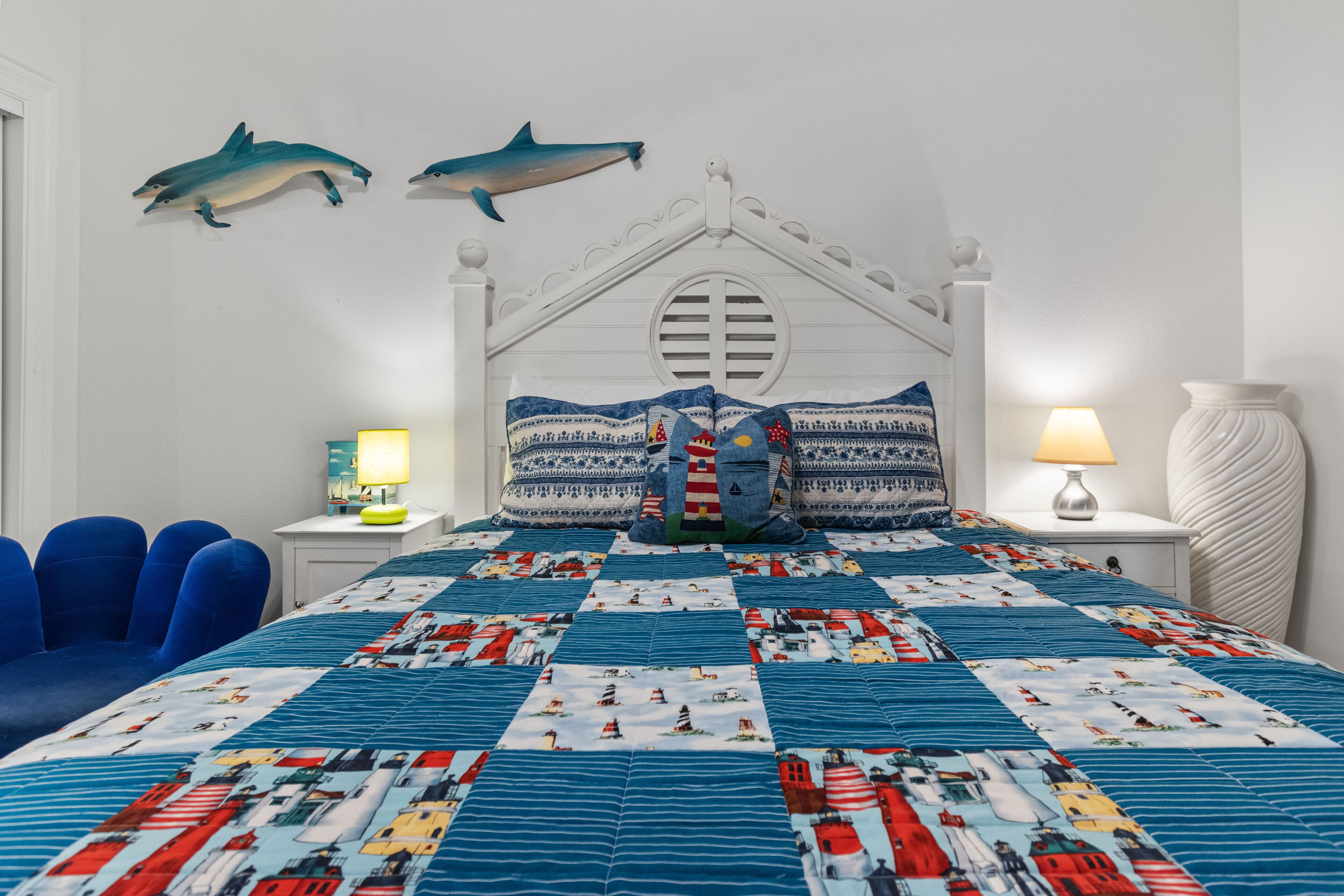 Ein Schlafzimmer mit einem Bett, blauen Stühlen, einem Nachttisch mit Lampe und zwei Wanddekorationen mit Delphinen.
