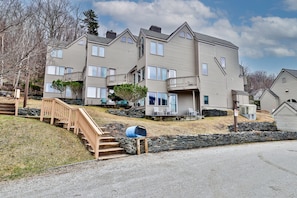 A multi-story residential building with a stone retaining wall, a wooden staircase, and a mailbox.