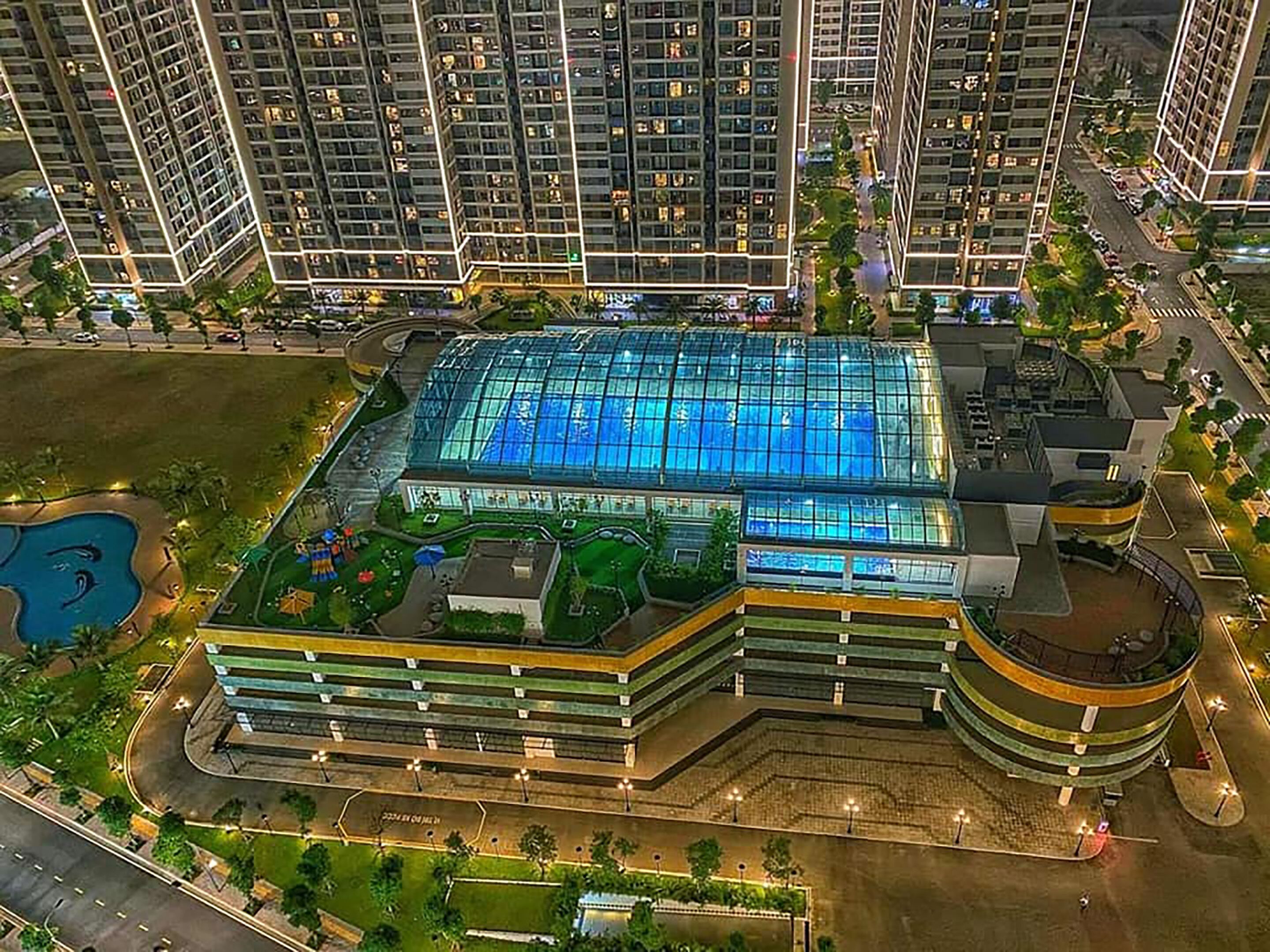 Un edificio de gran altura con una amplia piscina cubierta de vidrio y un área de azotea ajardinada.