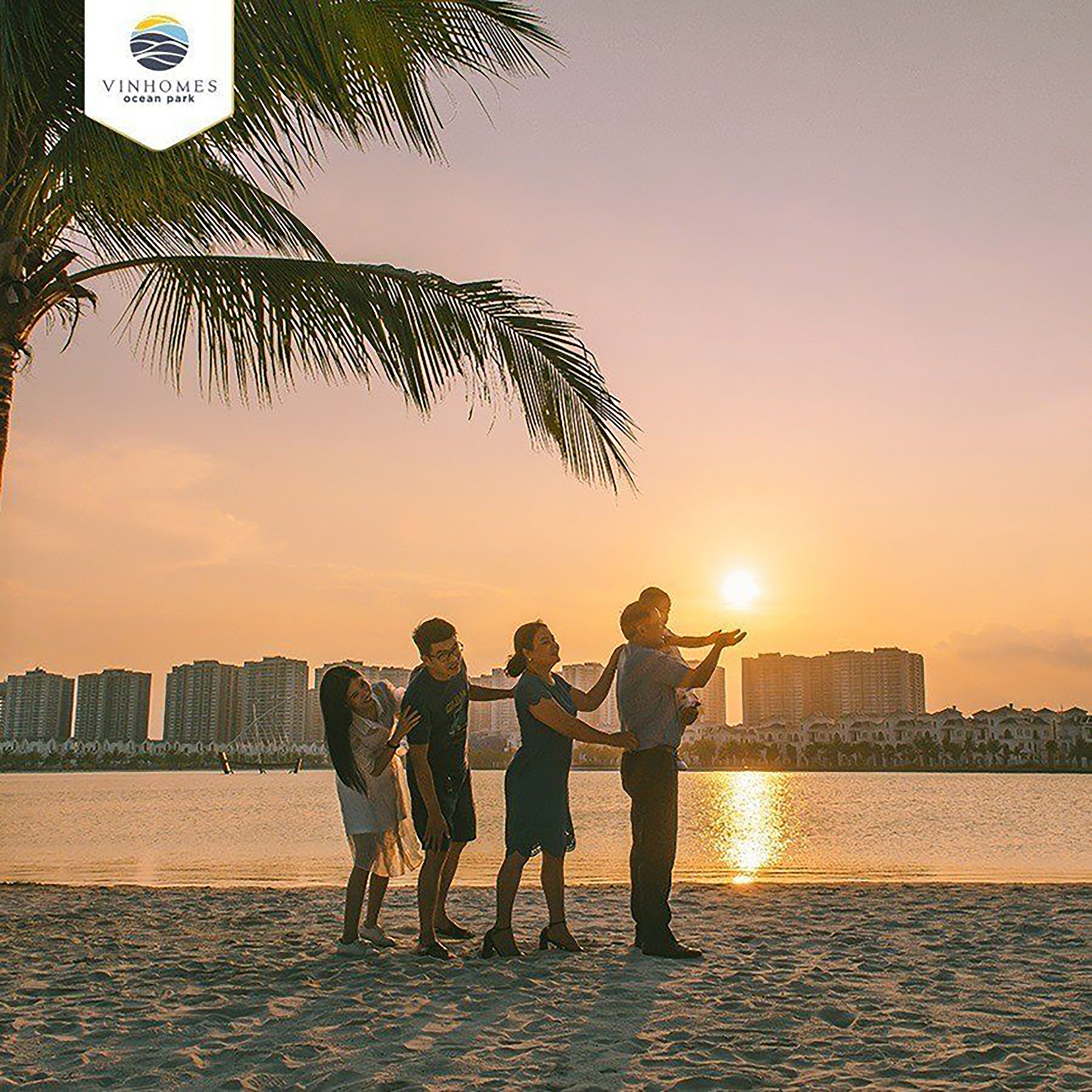 A sunset view with a group of people on a beach, palm trees, and a city skyline in the background.