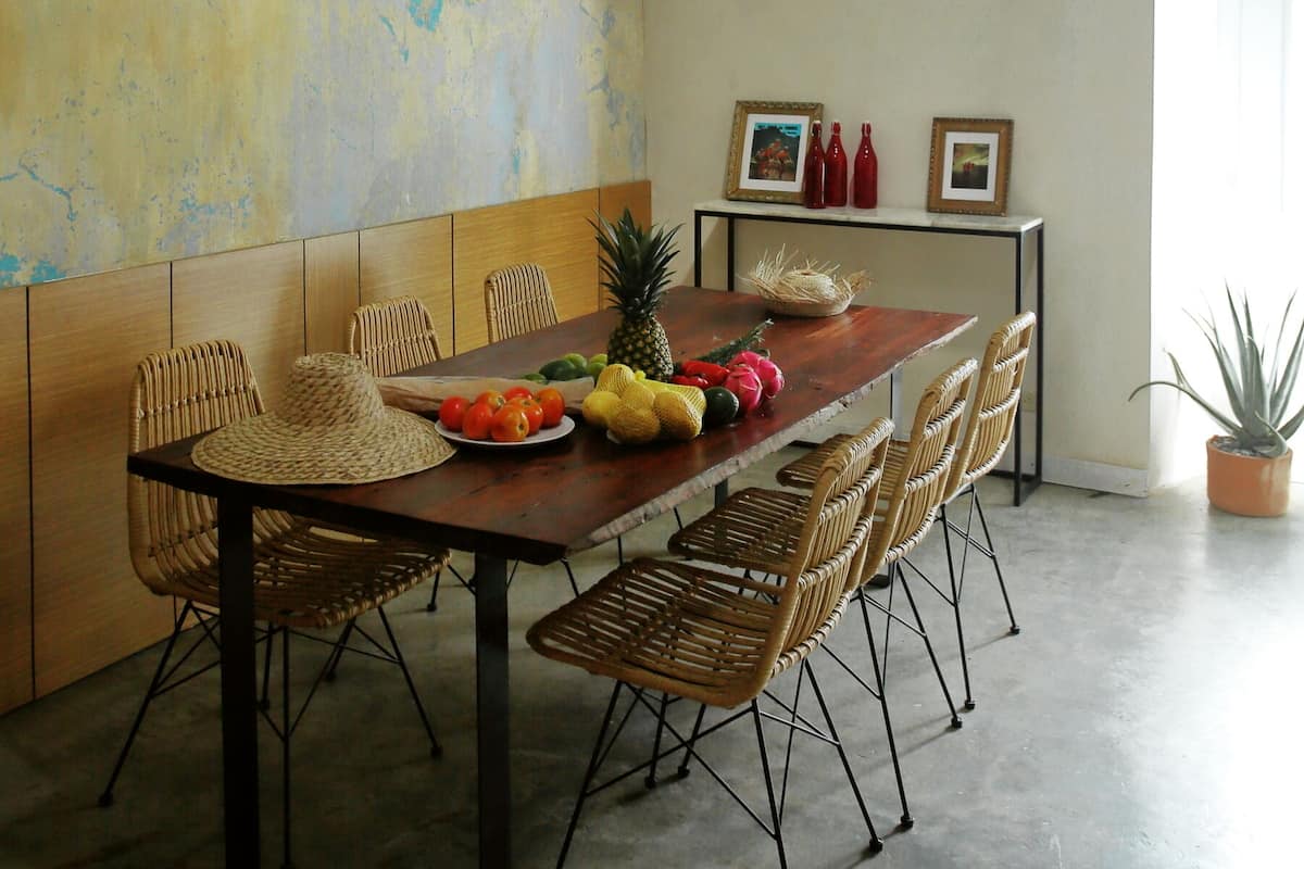 A dining area with a wooden table, wicker chairs, and a hanging light fixture.