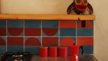 A kitchen with a gas stove, red gas cylinders, and a red coffee pot on a black countertop.