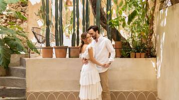 Una pareja parada sobre una plataforma de madera con una piscina al frente, rodeada de cactus y plantas en macetas.