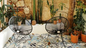 Un patio con dos sillas de alambre negras, un suelo de baldosas estampadas y una pared de ladrillo rústico con cactus.