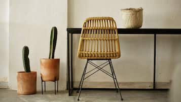 A wicker chair with a woven backrest and metal legs, a small potted cactus, and a woven basket on a black table against a plain wall.