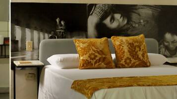 A bedroom with a bed, a nightstand, a wooden bench, and a large poster on the wall.