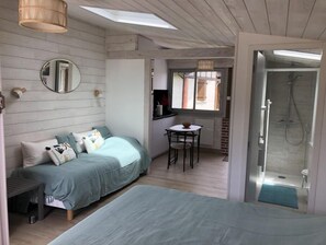 Cozy retreat with a single bed, compact kitchenette, and bathroom featuring a glass-enclosed shower.
