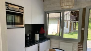 A compact kitchen with a built-in oven, a coffee maker, and a window overlooking a house.