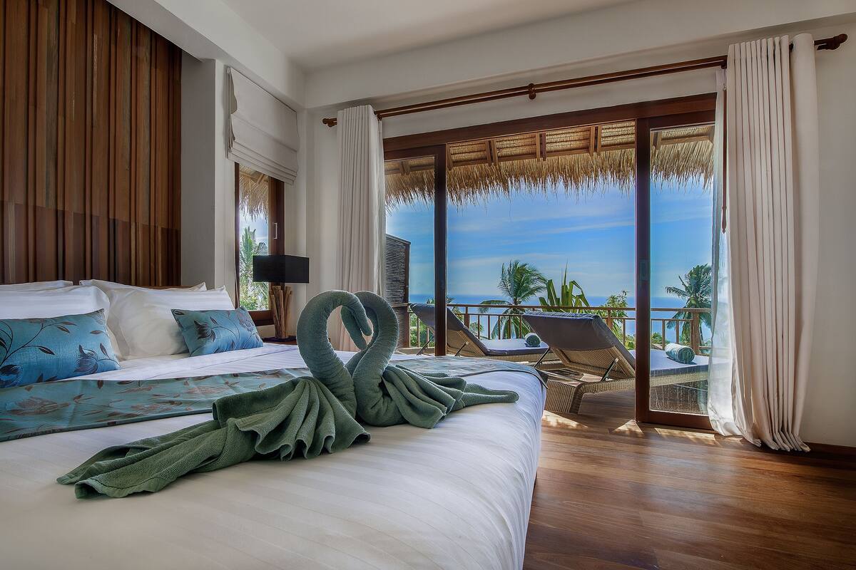 A hotel room with a bed, a view of the ocean, and a balcony with a chair.