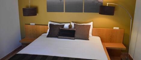 A neatly made bed with a striped blanket, a headboard with built-in shelves, and a wall-mounted artwork depicting a landscape.