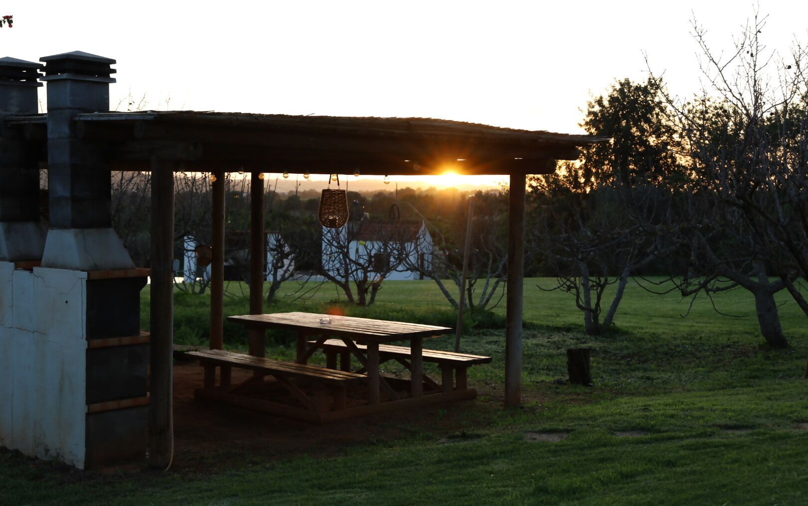 A wooden picnic table under a shelter with a view of a house and trees in the background.