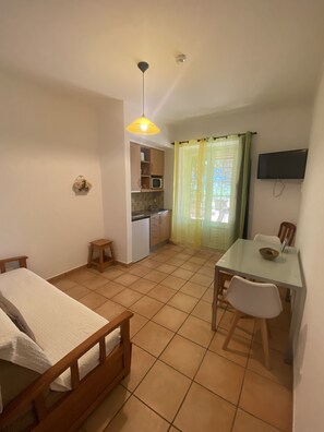 Et kompakt værelse med seng, et lille bord med stol, tekøkken og et fjernsyn ophængt på væggen.