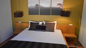 A neatly made bed with a striped blanket, a headboard with built-in shelves, and a wall-mounted artwork depicting a landscape. - 1-Bedroom apartment "Oliveira" – Pool view (2 + 2) (Mesquita)