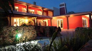 A two-story house with a red facade, a stone wall in the foreground, and a clear sky at dusk. - 1-Bedroom apartment "Oliveira" – Pool view (2 + 2) (Mesquita)