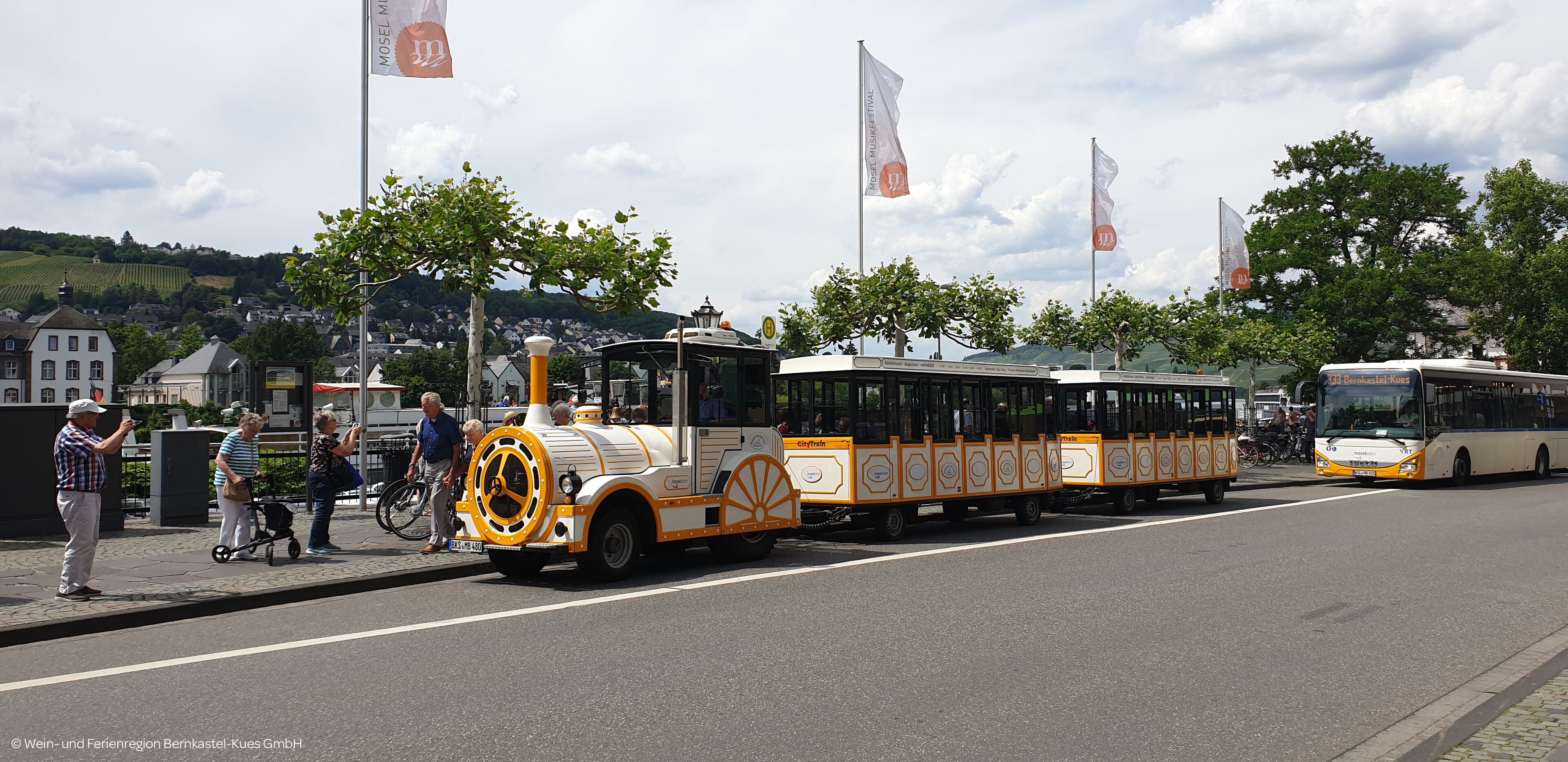 A tram with a clock face on the front, parked on a street with people around.