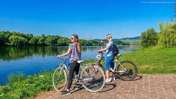 Dos personas están de pie junto a bicicletas, cerca de un río con un puente al fondo.