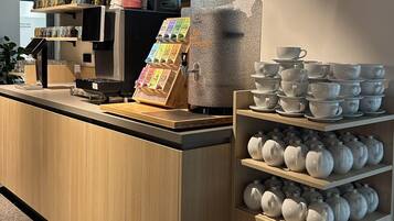 A coffee shop counter with a coffee machine, a menu board, and shelves with cups and teapots.