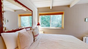 A bedroom with a large bed, two windows with blinds, a red lamp, and a mirror on the wall.