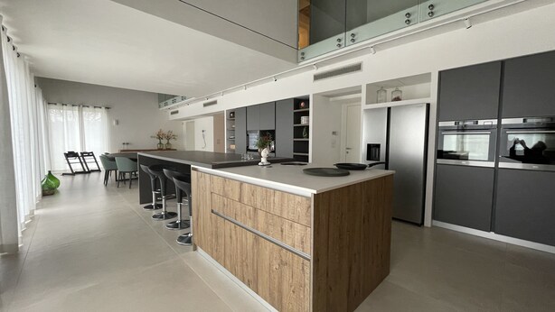 Een moderne keuken met een centraal eiland, barkrukken en inbouwapparatuur.