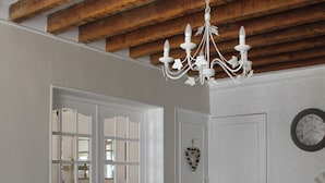 A dining area with a wooden ceiling, white chairs, a dark table, and a chandelier.