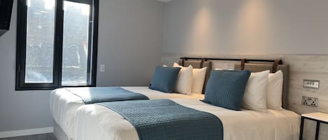 A modern bedroom with a large bed, two bedside tables, and a window with a view of trees.
