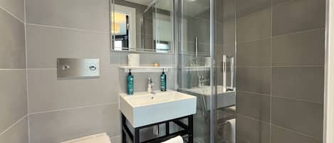 Um banheiro moderno com pia branca, box de vidro e porta-toalhas.