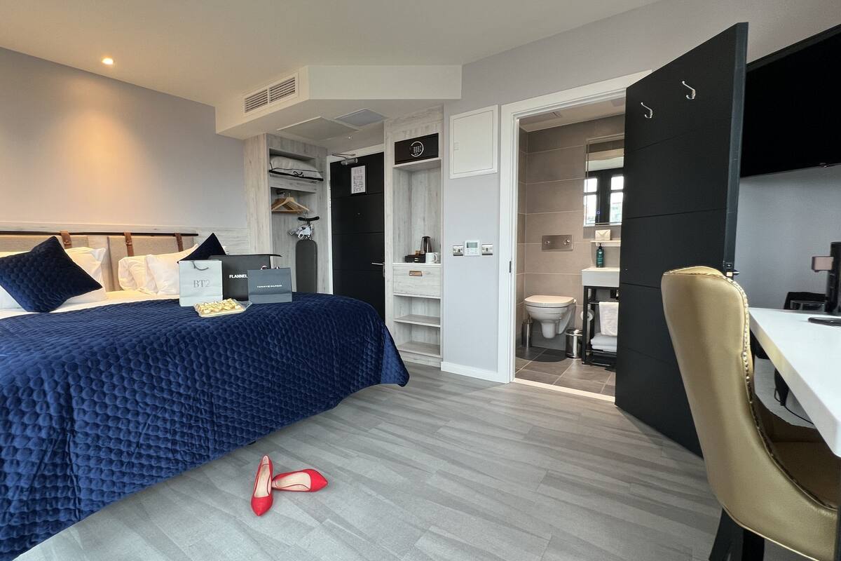 A modern bedroom with a bed, a desk, and a bathroom visible through an open door.