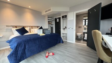 Un dormitorio moderno con cama, escritorio y baño a la vista a través de una puerta abierta.