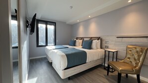 A modern bedroom with a large bed, a side table, a gold chair, and a window with a view of the city. - Wellington Temple Bar (Dublin)