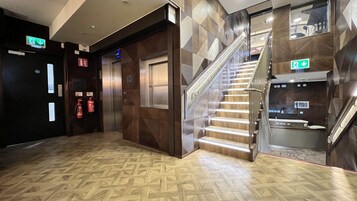 Vestíbulo de hotel con piso de diseño espiga, escalera con barandales de metal y equipo de seguridad contra incendios.