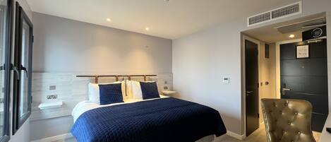 A modern bedroom with a bed, a chair, a bedside table, and a window.