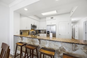 Une cuisine moderne avec des armoires blanches, des appareils en acier inoxydable, un comptoir en granit et des tabourets de bar en bois.