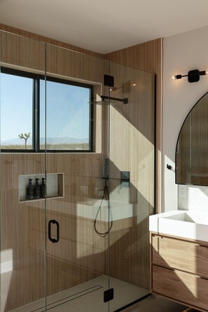A modern bathroom with a glass-enclosed shower, a large window, and a vanity with a mirror.
