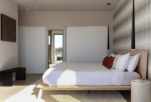 A modern bedroom with a large bed, a bench, and a view of the outdoors.