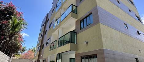 A multi-story building with balconies, a paved walkway, and some greenery.