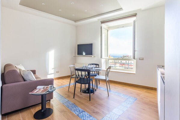 Un soggiorno moderno con un divano, un tavolo da pranzo con sedie, una TV a parete e un'ampia finestra con vista.