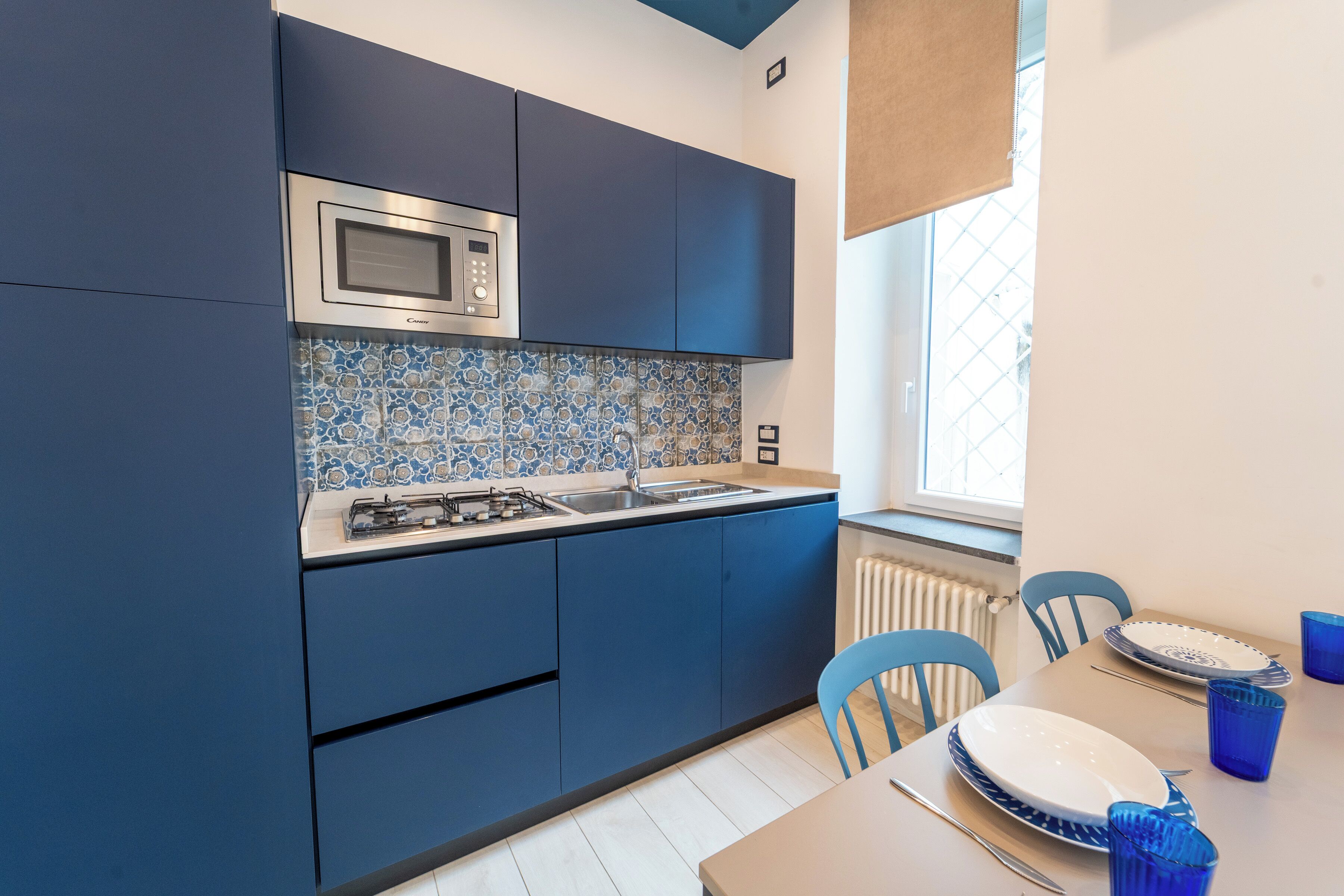 Een moderne keuken met donkerblauwe kastjes, een roestvrijstalen magnetron en een betegelde spatwand.